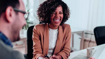 Três pessoas sorrindo em uma reunião de trabalho.