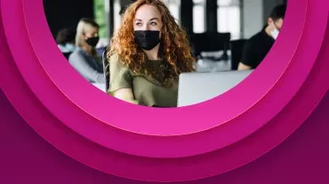 Pessoa de máscara em local de trabalho, com fundo rosa.