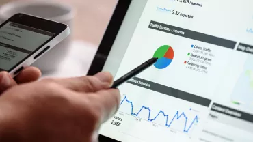 Pessoa analisando gráficos em tablet e smartphone.