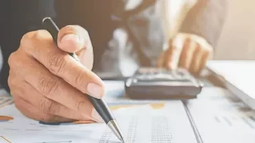 Pessoa usando caneta e calculadora em escritório.