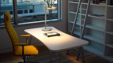 Escritório iluminado com cadeira amarela e prateleiras vazias.