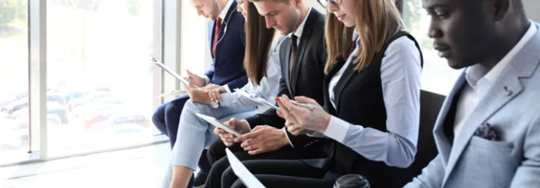 Pessoas sentadas em uma sala, segurando documentos e usando celulares.