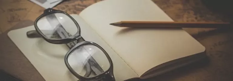 Óculos e lápis sobre um caderno aberto em cima de um mapa antigo.
