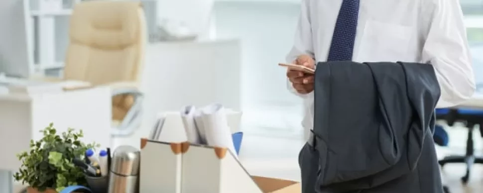 Pessoa em escritório com caixa de objetos pessoais na mesa.